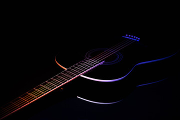 Fototapeta na wymiar black guitar on a dark background under beam of colored light with copy space. guitar music low-key concept diagonal projection