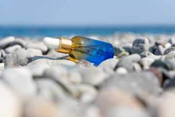 A dropper bottle of face serum or natural oil lying on the stones on the beach