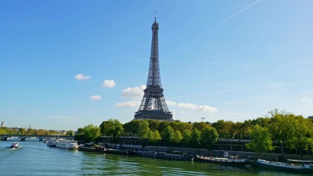 View of the Eiffel Tower and the bridge from the Seine River. Boats sail along the river, elevators run in the tower. Timelapse video on a sunny summer day. Paris, France.