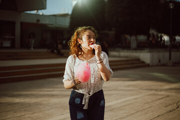 Fototapeta premium mujer degustando Algodón de Azúcar en un parque mientras esta de vacaciones.