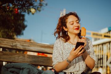 Mujer disfrutando un helado mientras mira su celular. Concepto de vacaciones y tecnología.