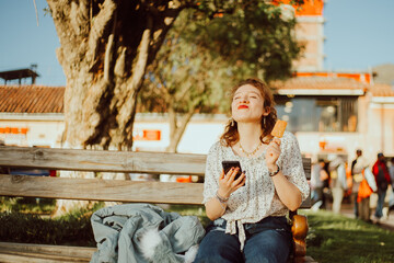 Mujer disfrutando de sus vacaciones comiendo una paleta y mirando su celular. Concepto de Turismo,...