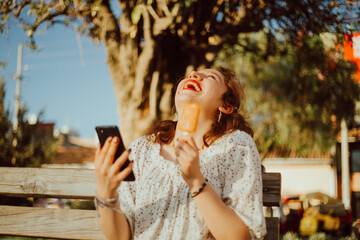Mujer disfrutando de sus vacaciones comiendo una paleta y mirando su celular. Concepto de Turismo,...