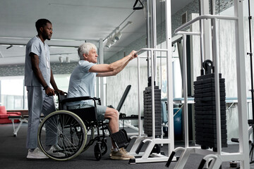 Side view portrait of senior man in wheelchair using exercise machines at rehabilitation clinic, copy space