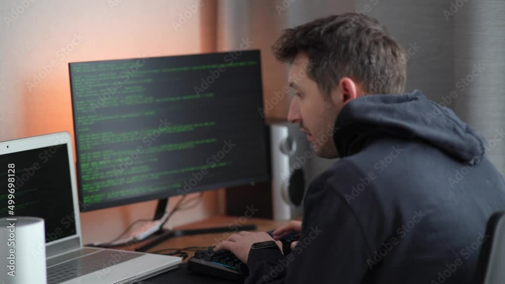 Wall mural a hacker in a hood types program code. young man criminal wearing black hoodie, typing on keyboard. 