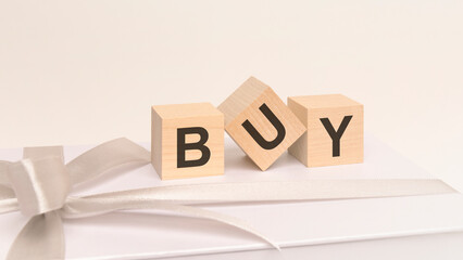 three cubes with text Buy on the white surface of a gift box tied with a light festive ribbon