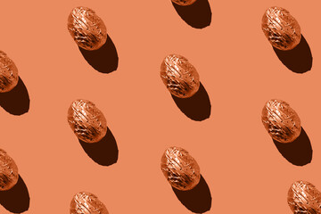 Easter eggs pattern in golden aluminum foil on coral background. Easter holiday creative concept.