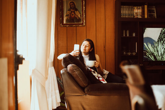 Mujer joven tomando caf&eacute; y mirando su tel&eacute;fono. Concepto de tecnolog&iacute;a y hogar. 