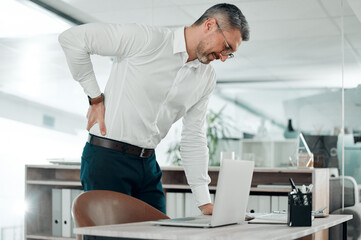 Ooo, my back is killing me. Shot of a mature businessman standing alone in his office and suffering from backache.