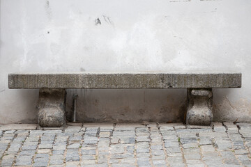 Stone bench with old wall on background and cobblestone on street