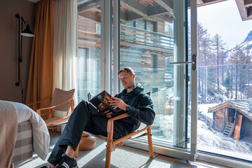 Tourist reading journal while relaxing in bedroom at luxurious ski resort