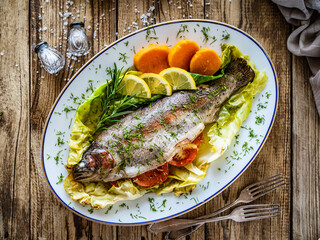 Roast trout with potatoes and tomatoes on green cabbage leaves served on wooden table