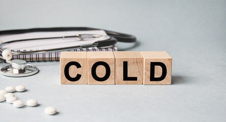 COLD inscription on wooden cubes isolated on white background, medicine concept. Nearby on the table are a stethoscope and pills.