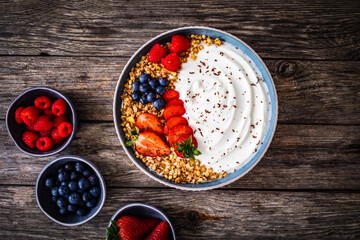 Yogurt with strawberries, blueberries, raspberries and muesli in bowl on wooden table