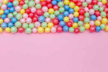 Multi-colored round glossy balls of sugar confectionery topping lie at the top on a pink background.