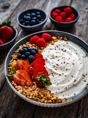 Yogurt with strawberries, blueberries, raspberries and muesli in bowl on wooden table