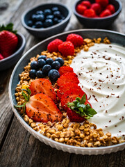 Yogurt with strawberries, blueberries, raspberries and muesli in bowl on wooden table