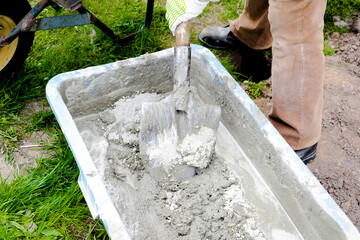 Worker man mixing, stirring cement slurry, concrete rubble mortar with shovel in big bowl, reservoir, trough, bucket. Preparing for building process, renovation, laying foundation