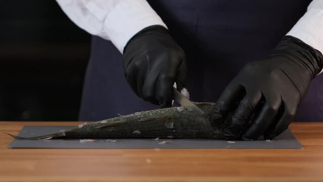 Cleaning fresh mullet fish from scales hands with a knife on cutting board closeup. Unrecognizable cook cleans the fish. Cooking fish at home. Dishes from sea fish. Delicacy healthy food concept, slow