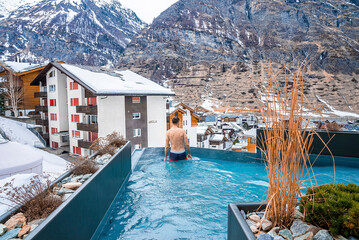 Tourist swimming in pool while looking at snow covered houses and mountain