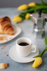 Chic espresso and croissant breakfast with yellow tulips.