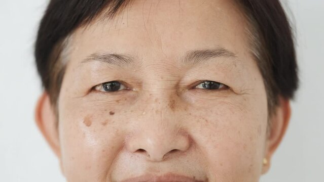 Close-up of eyes of mature asian senior woman smiling to camera. Face close up of attractive old woman from Thailand with dark spots on her skin. Nationality Diversity, Ethnicity Differences