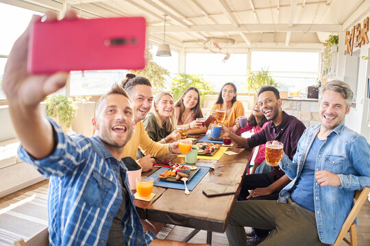 Man taking mobile phone selfie with a multiracial group of friends in a bar.