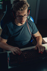 Young blond guy playing video games, playing on his laptop in the dark illuminated by the screen.