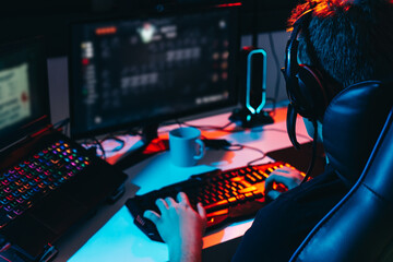 Young man addicted to video games playing on a computer with headphones. Young gamer illuminated with coloured lights