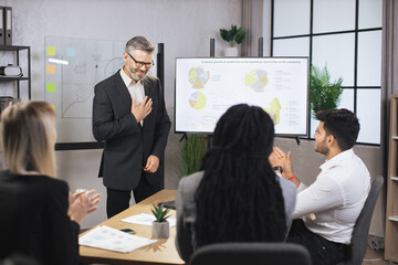 Business concept. Successful confident experienced diverse team of corporative workers, listening mature male expert, showing strategy of company, financial reports on the wall TV screen.