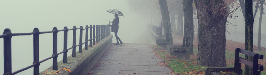 Beautiful woman with umbrella walking in the rain on a misty autumn day