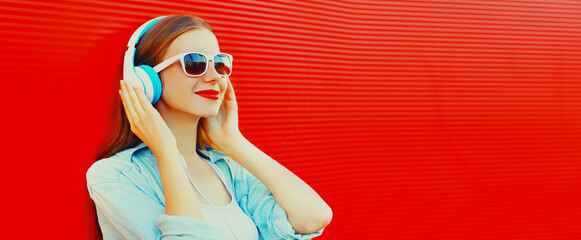 Portrait of happy smiling young woman with headphones listening to music on red background, blank copy space for advertising text