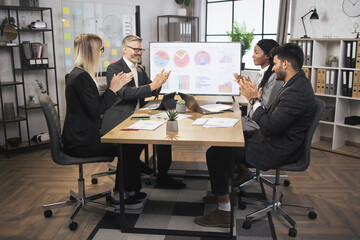 Good results, business, congratulation and appreciation concept. Two satisfied diverse business men and women in formal wear, sitting at the table in conference hall and applauding. Focus on young man