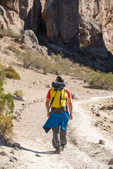 Back view of tourist with yellow backpack walking among rocky mountains.