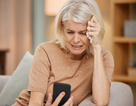 Please tell me this isnt true. Shot of a mature woman using a smartphone and crying on the sofa at home.