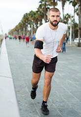 Athletic young man in a white shirt running and listening to music on headphones.