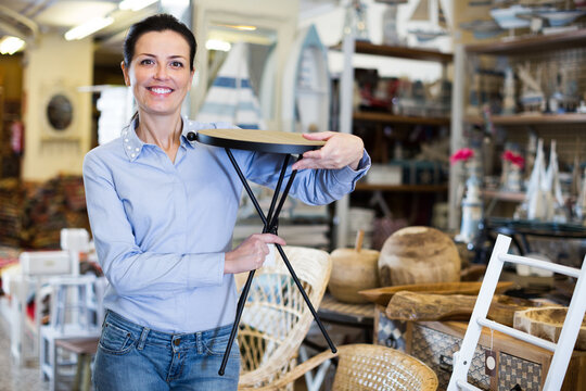 Smiling woman holding chair before buying at the local interior store