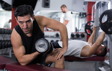 Concentrated sporty guy during workout in gym with dumbbells