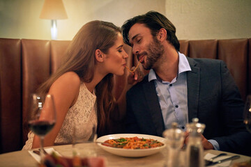 Love bites. Shot of a young couple sharing spaghetti during a romantic dinner at a restaurant.