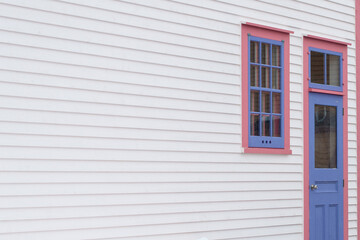 The exterior wall of a white wooden cape cod clapboard siding house with a purple panel door and...