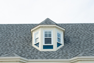 A pyramidal roof dormer with three small closed glass windows outward facing. The house is green...