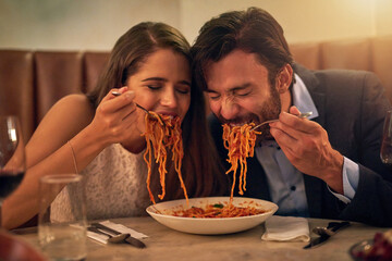 Love is all consuming. Shot of a young couple sharing a plate of spaghetti during a romantic dinner at a restaurant.