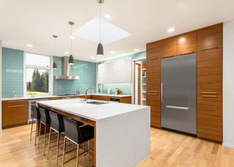 Beautiful modern kitchen in new luxury home. Features quartz waterfall island, elegant cabinets, hardwood floors, skylight, stainless steel appliances, and counter to ceiling tile backsplash. 