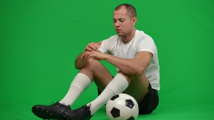 Desperate Caucasian footballer sitting with soccer ball on green screen sighing holding head in hands. Wide shot portrait of sad unsatisfied sportsman at chromakey background. Failure and sport