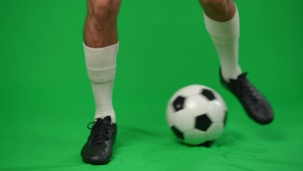 Legs of young professional footballer dribbling ball at chromakey background. Unrecognizable Caucasian sportsman training on green screen stopping putting foot on soccer ball