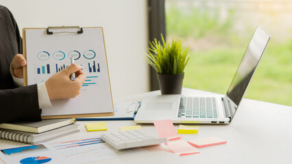 Businessman or accountant holding pen and analytical chart papers calculate company budget and financial planning turnover rate with graph report and use laptop computer for data analysis.