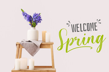 Vase with beautiful hyacinth flowers and candles on stand against light background. Welcome, spring