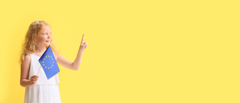 Little girl with flag of European Union pointing at something on yellow background with space for text - Powered by Adobe