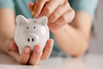 Female hand putting money into piggy bank for saving money. Saving money and increasing finances concept.