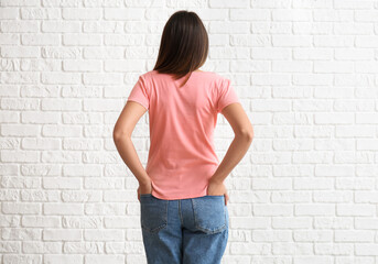 Young woman in blank t-shirt on white brick background, back view